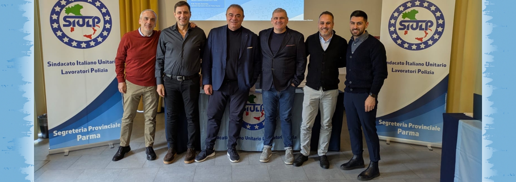 Sei rappresentanti del SIULP in piedi davanti ai roll-up del sindacato durante il convegno con Felice Romano, 2025.